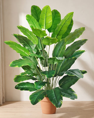 Artificial banana leaf plant in a plain terracotta pot against a warm off-white plaster wall