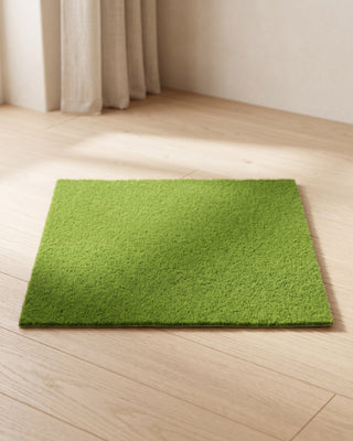 An artificial grass mat laid flat on pale oak floorboards in a bright, calm room