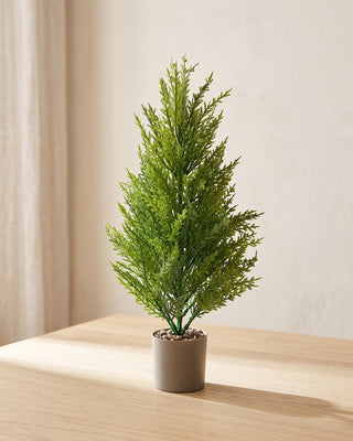 An artificial pine tree in a plain nursery pot on a pale oak table in a bright room; pot not included