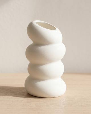 A spiral bud vase in matte white, empty, on a pale oak table