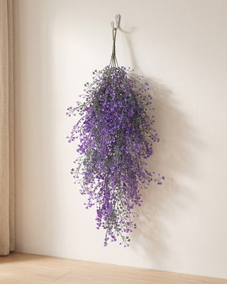 An artificial wisteria spray hanging from a simple hook on a pale wall, its full drop clear of the floor