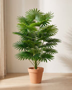 Artificial fan palm, a dense head of pleated fan-shaped fronds, standing in a plain terracotta pot on a pale oak floor (pot not included).