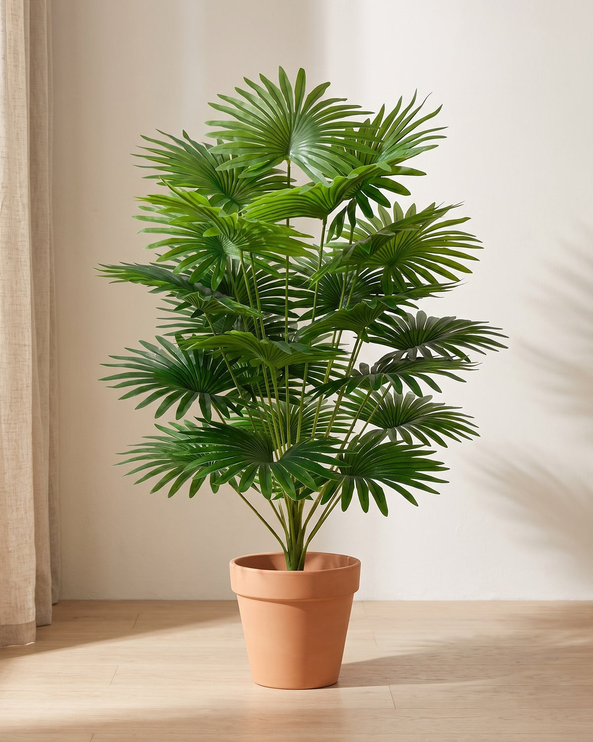 Artificial fan palm, a dense head of pleated fan-shaped fronds, standing in a plain terracotta pot on a pale oak floor (pot not included).