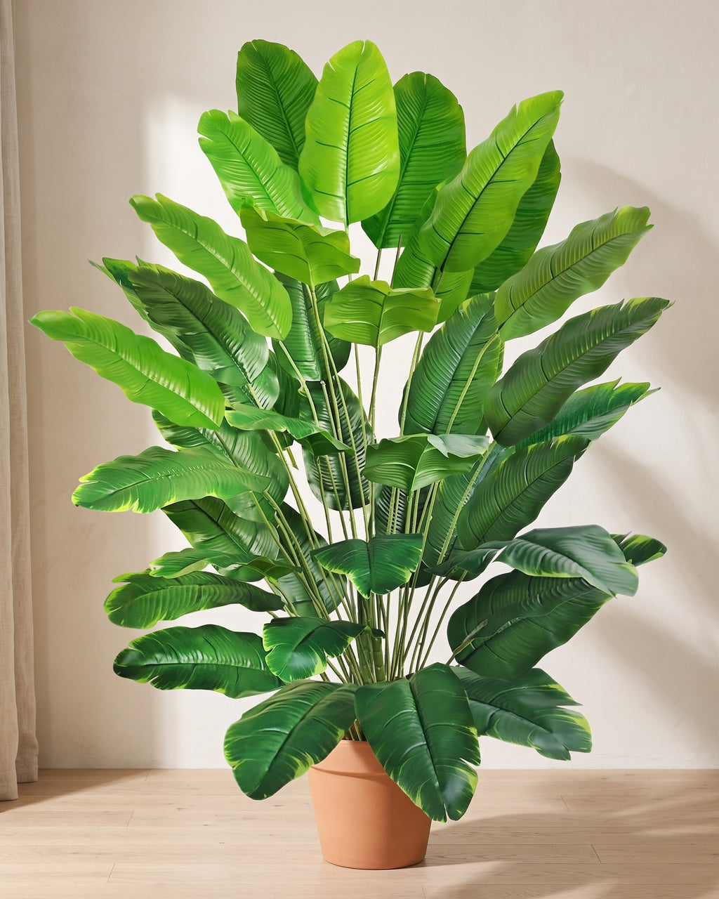 Artificial banana leaf plant in a plain terracotta pot against a warm off-white plaster wall
