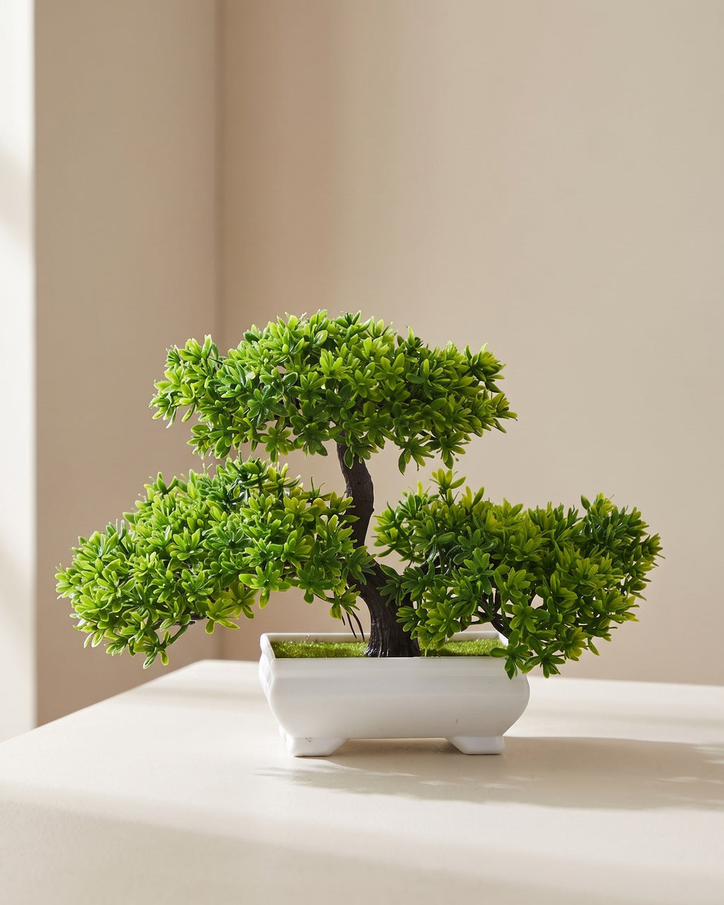 Artificial flowering bonsai in its plain white molded pot on a pale surface, canopy wider than the tree is tall
