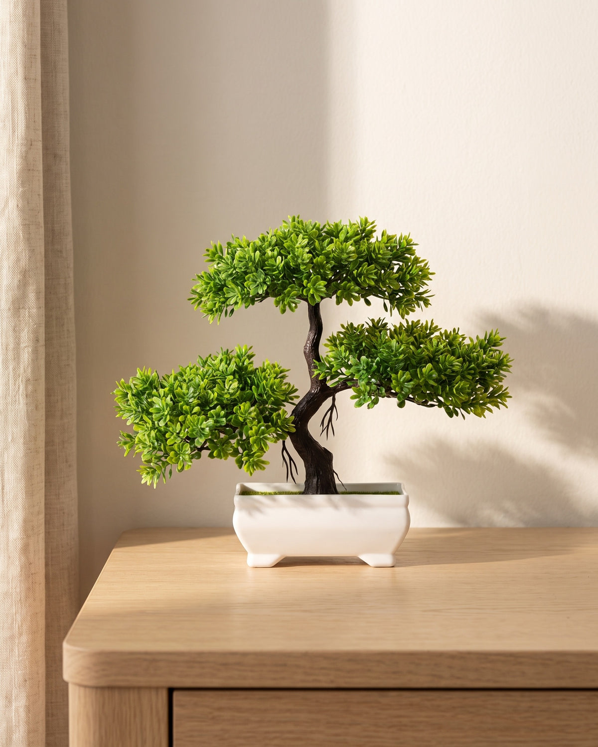 Small artificial bonsai in a white ceramic tray on a pale oak tabletop