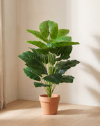 The 39.4 in artificial elephant ear plant in the corner of a bare room, shown in a plain terracotta pot (pot not included).