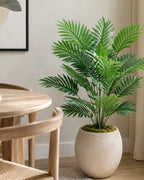 Artificial areca palm in a pale planter next to a wooden dining table