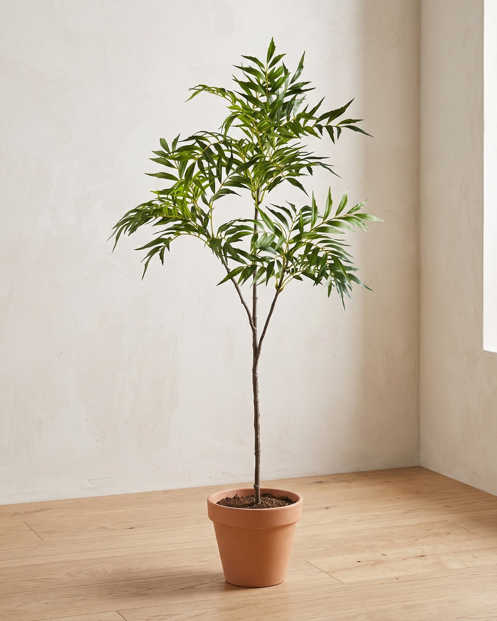 The artificial bamboo branch in the corner of a bare room, shown in a plain terracotta pot (pot not included).