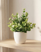 Mini artificial potted plant in a matte white pot on an oak shelf in soft daylight, coin leaf style