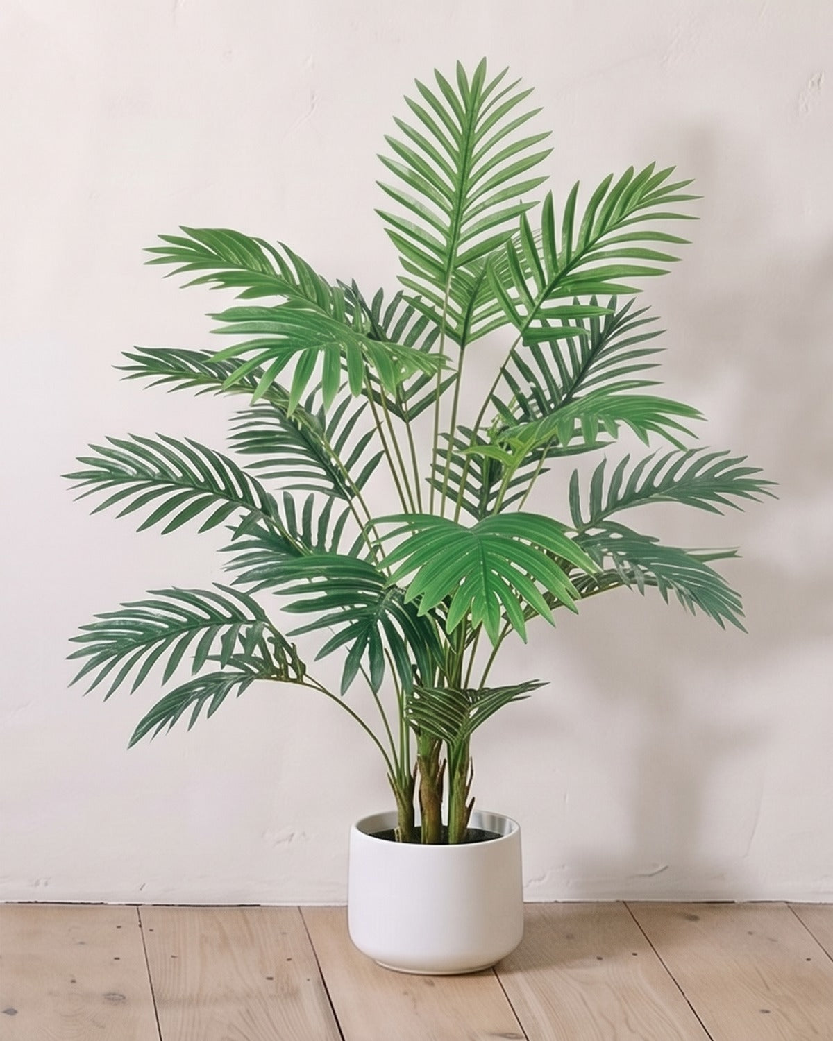 An artificial areca palm with twenty-four fronds, 35 in tall, in a plain white pot against a warm white wall; pot not included