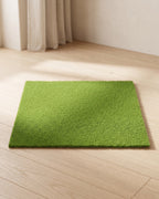 An artificial grass mat laid flat on pale oak floorboards in a bright, calm room