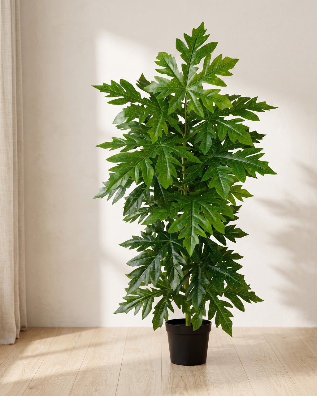An artificial papaya leaf plant in a plain nursery pot on pale oak floorboards in a bright room; pot not included