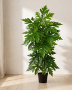 An artificial papaya leaf plant in a plain nursery pot on pale oak floorboards in a bright room; pot not included