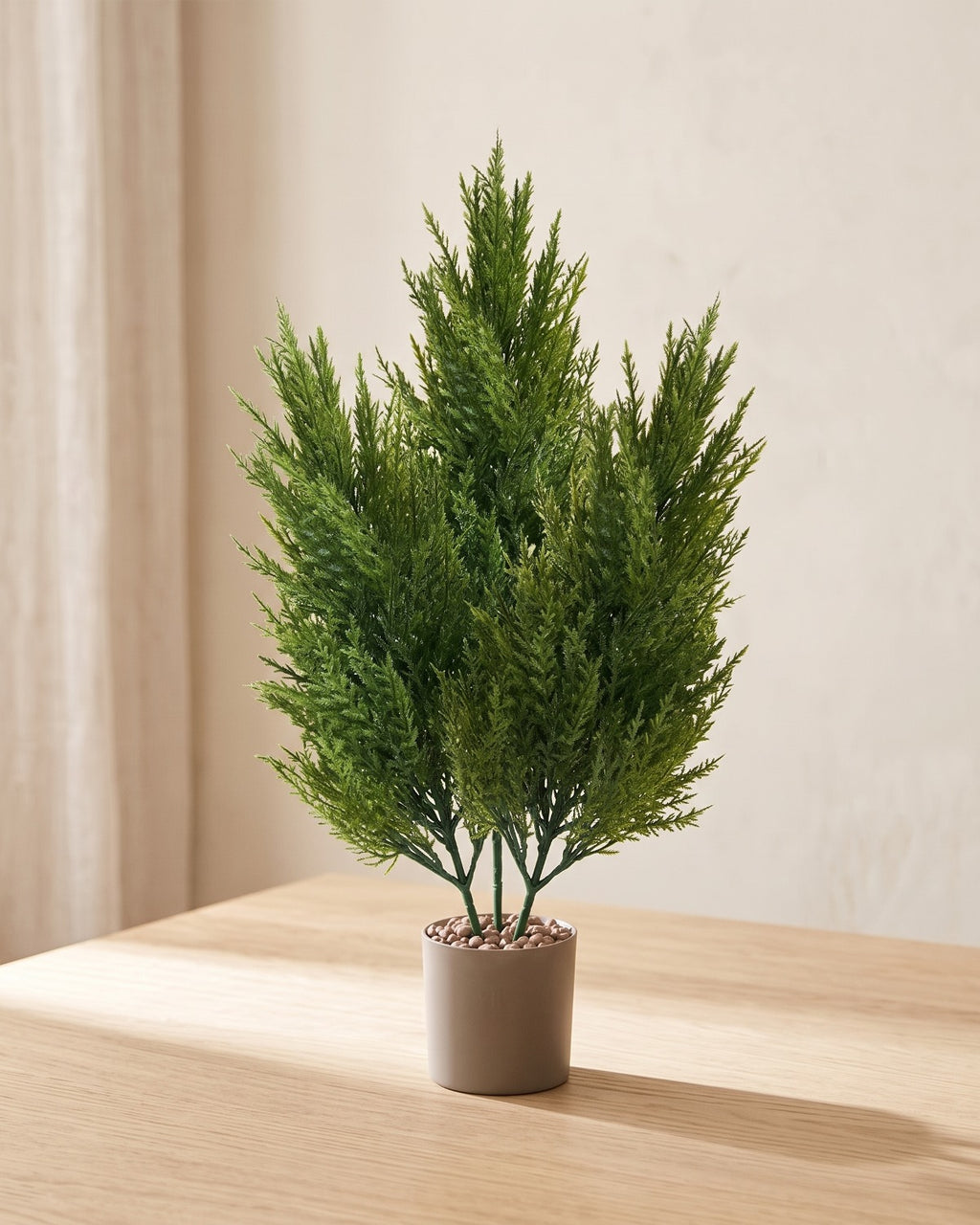 Three artificial pine bundles standing together in a plain nursery pot on a pale oak table; pot not included