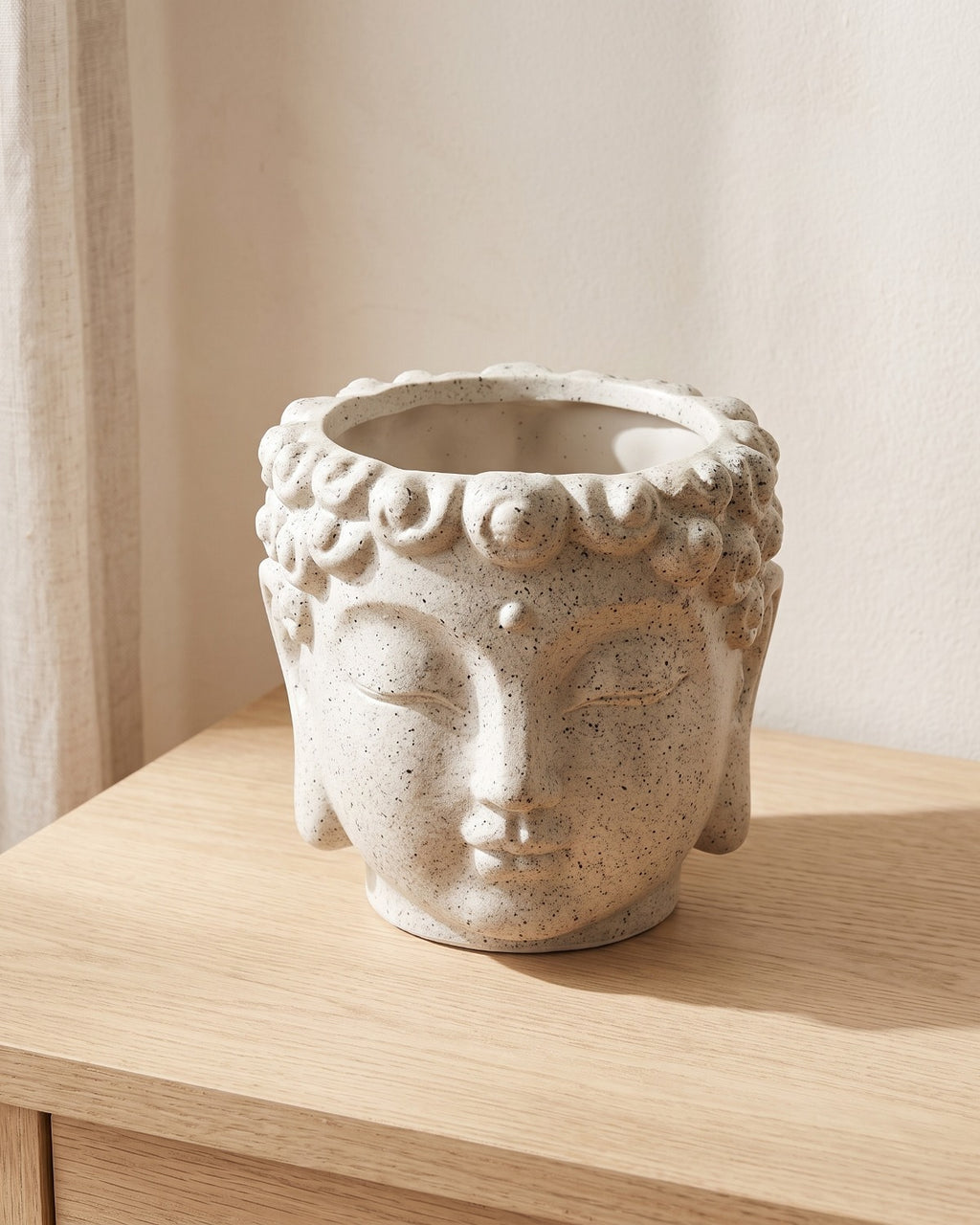 A stone Buddha head planter, empty, on a pale oak console