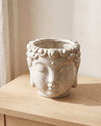 A stone Buddha head planter, empty, on a pale oak console