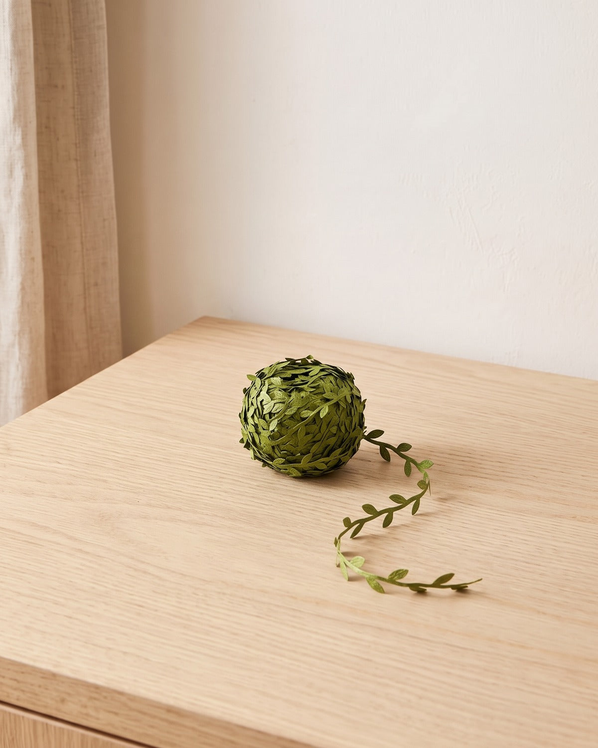 The 33 ft coil of artificial leaf trim wound into a ball, with a length of trim loose beside it, on a pale oak table