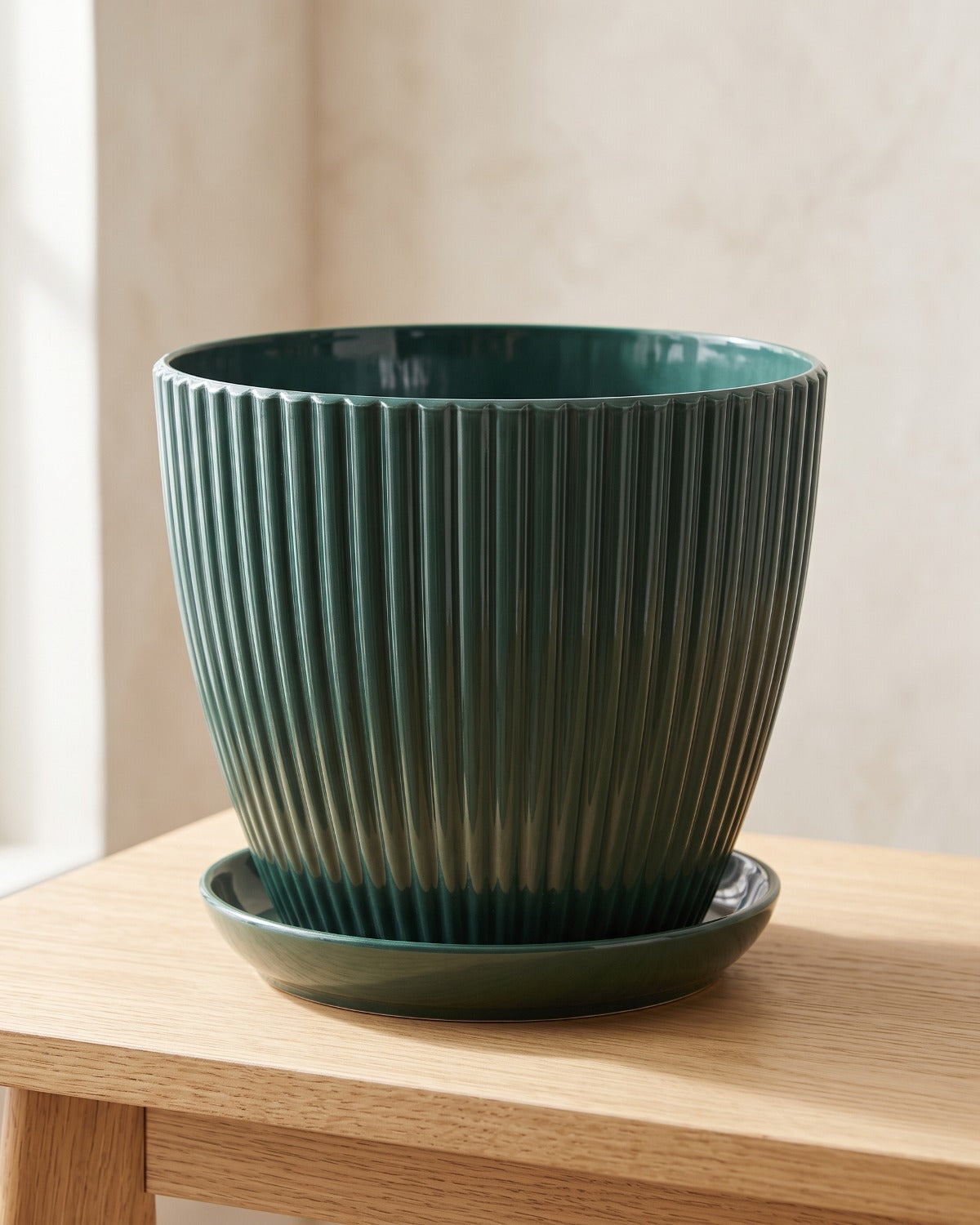 Forest green fluted plant pot and saucer, empty on a pale oak table