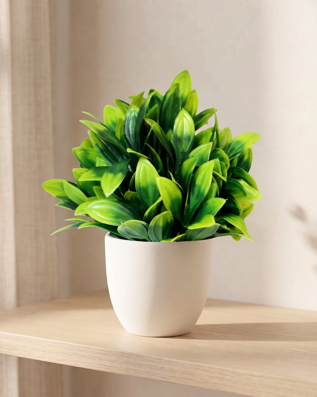 Dracaena style mini artificial potted plant in a plain white pot on a pale oak table