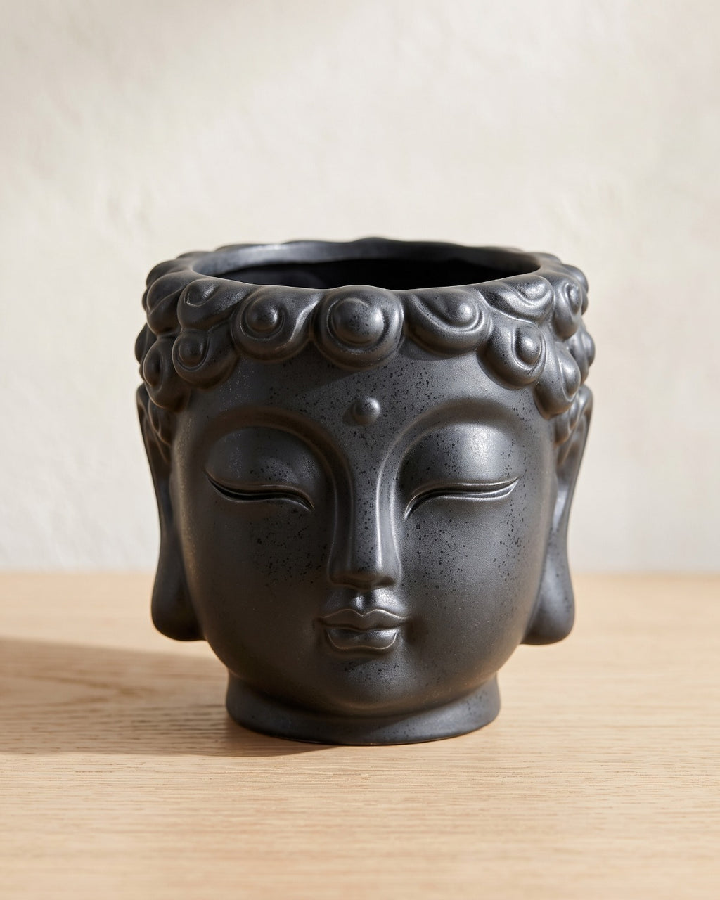Charcoal Buddha head planter, empty on a pale oak table