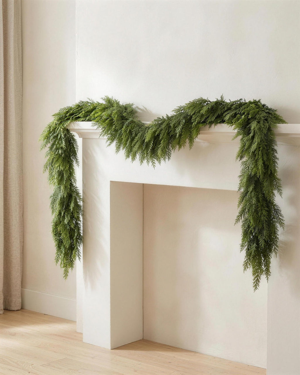 An artificial cypress garland draped along a white fireplace mantel