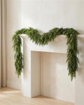 An artificial cypress garland draped along a white fireplace mantel