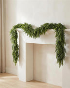 An artificial cypress garland draped along a white fireplace mantel