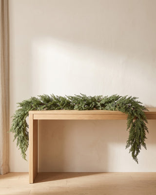 An artificial cedar garland laid along a pale oak console table