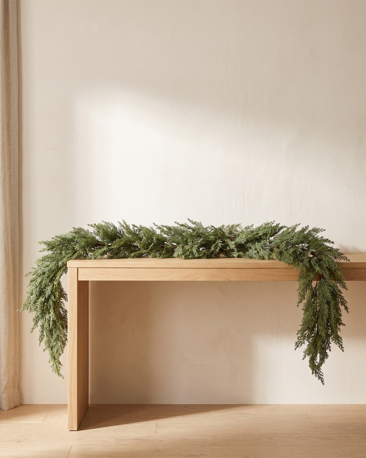 An artificial cedar garland laid along a pale oak console table