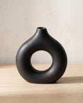 Black donut vase, small, empty on a pale oak table
