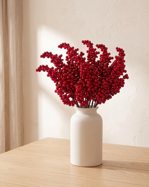 Twenty artificial red berry branches, a full bunch, in a plain off-white vase on a pale oak table; vase not included