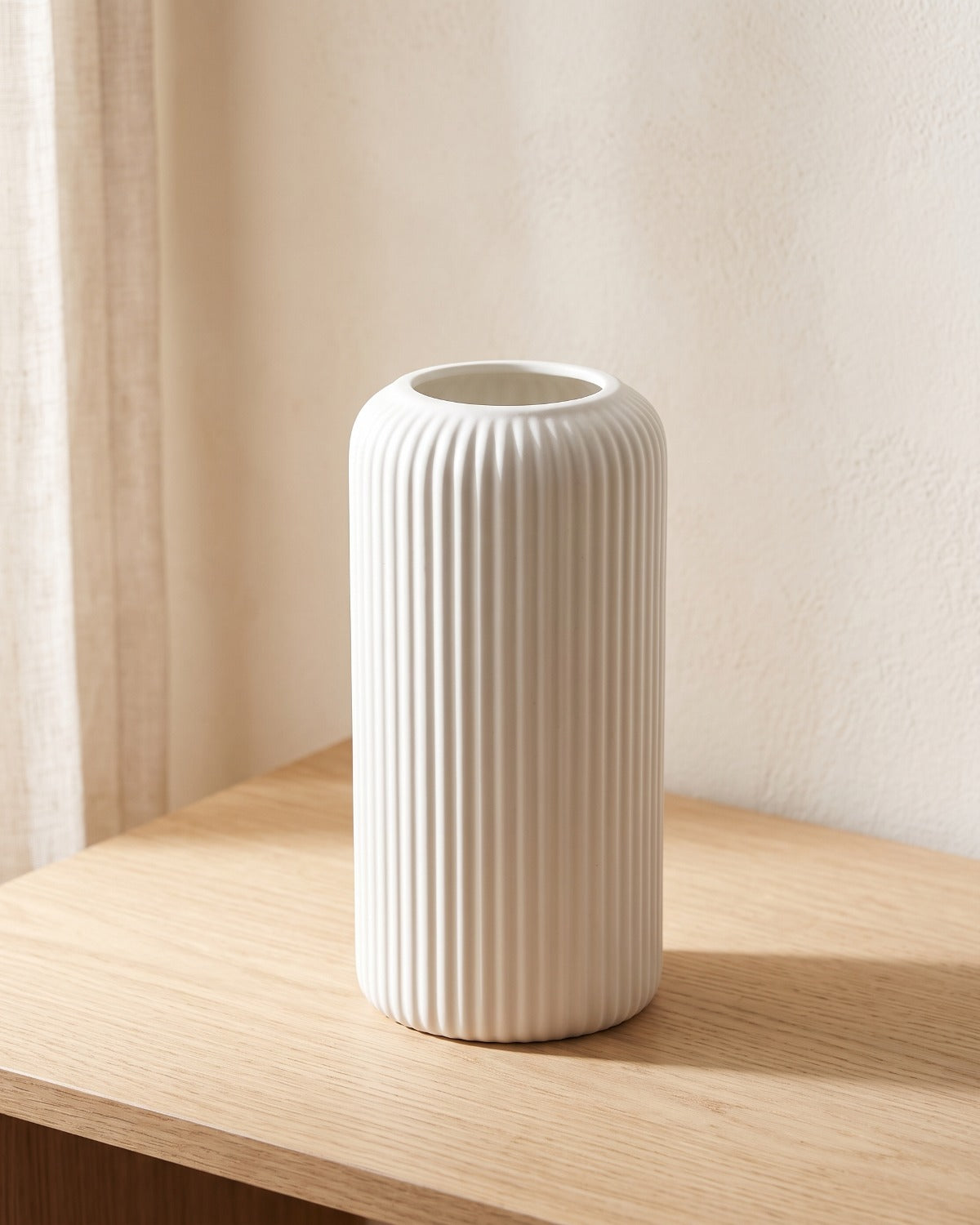 A white striped cylinder vase, empty, on a pale oak console