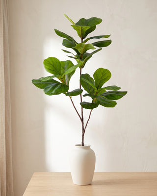 An artificial tree branch standing in a plain off-white vase on a pale oak table; each order is cut stems, and no vase is included