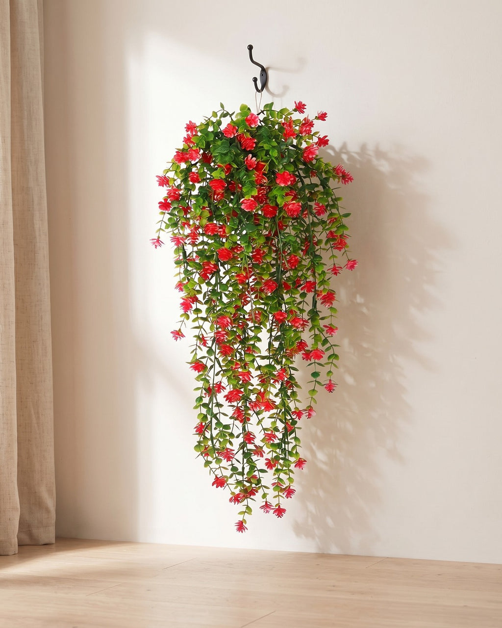 One artificial flowering hanging vine with red blossoms, on a black iron hook against a warm plaster wall; hook not included