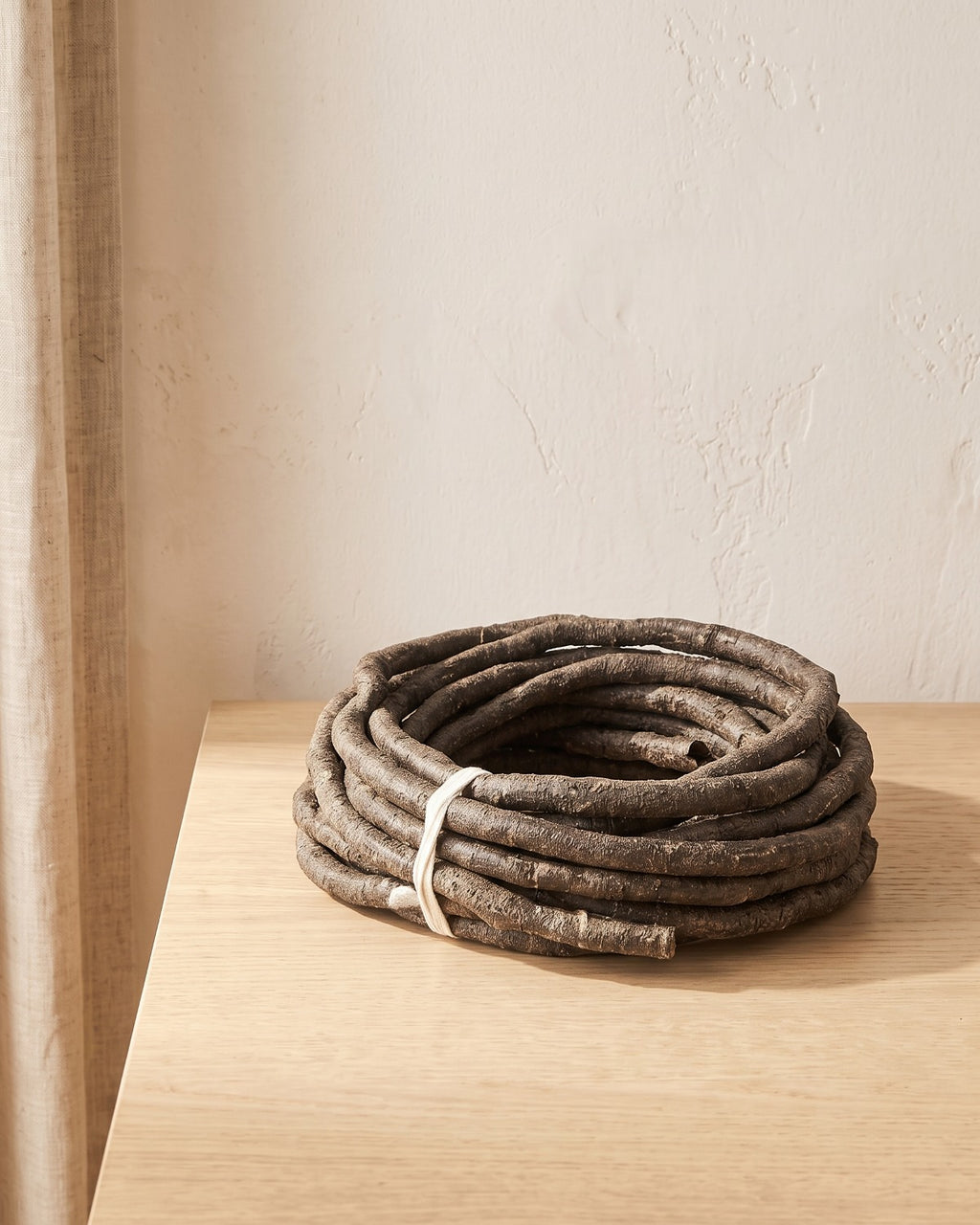 A coil of brown bark-textured artificial jungle vine at its 13 ft length, on a pale oak table