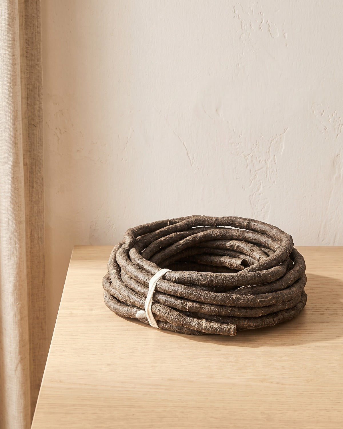 A coil of brown bark-textured artificial jungle vine at its 13 ft length, on a pale oak table
