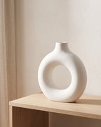 A white donut vase, empty, on a pale oak console