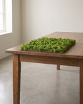 A square artificial moss mat lying on a wooden table, the smallest of the three sizes; table not included