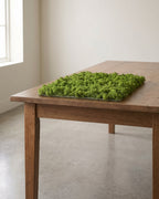 A square artificial moss mat lying on a wooden table, the smallest of the three sizes; table not included