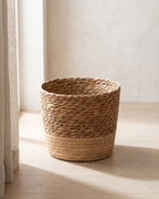 A woven seagrass plant basket, empty, on pale oak floorboards