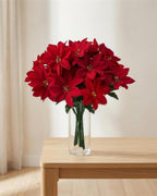 A red artificial poinsettia bouquet in a clear glass vase on a side table; vase not included