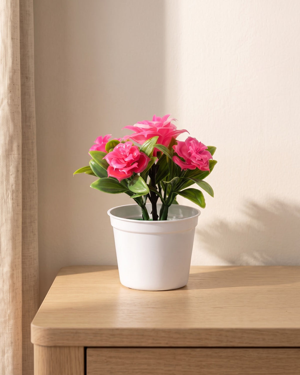 A small artificial flowering pot with bright pink blooms, in the white pot it comes in, on a pale oak table