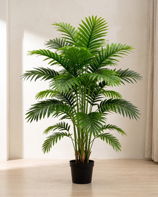An artificial palm leaf bush in a plain nursery pot on pale oak floorboards in a bright room; pot not included
