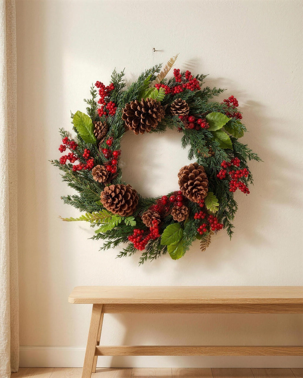 A cypress and pinecone Christmas wreath hanging on a plaster wall above a bench