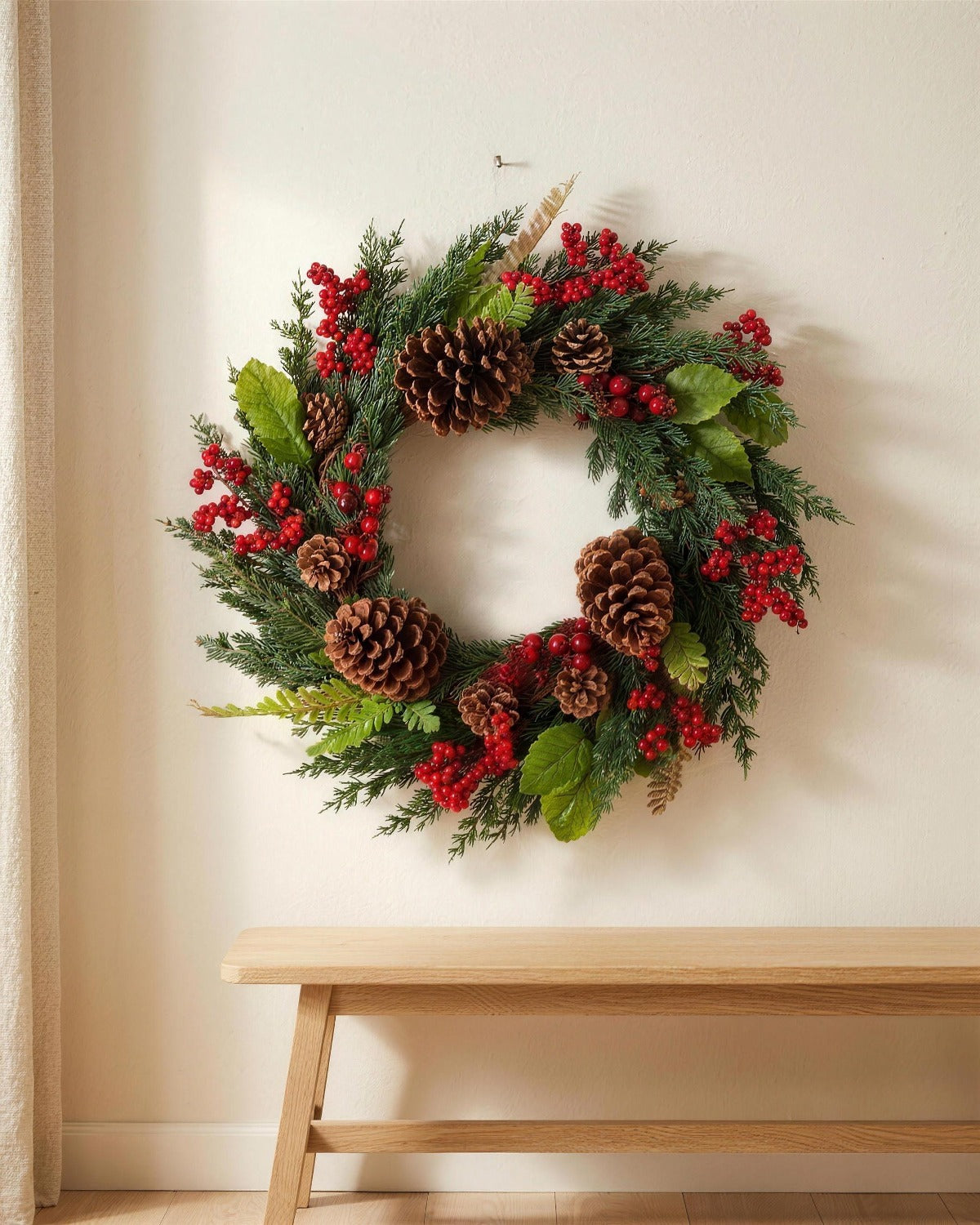 A cypress and pinecone Christmas wreath hanging on a plaster wall above a bench