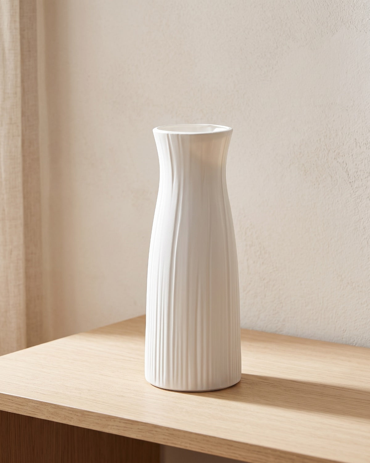 A fluted white origami vase, empty, on a pale oak shelf