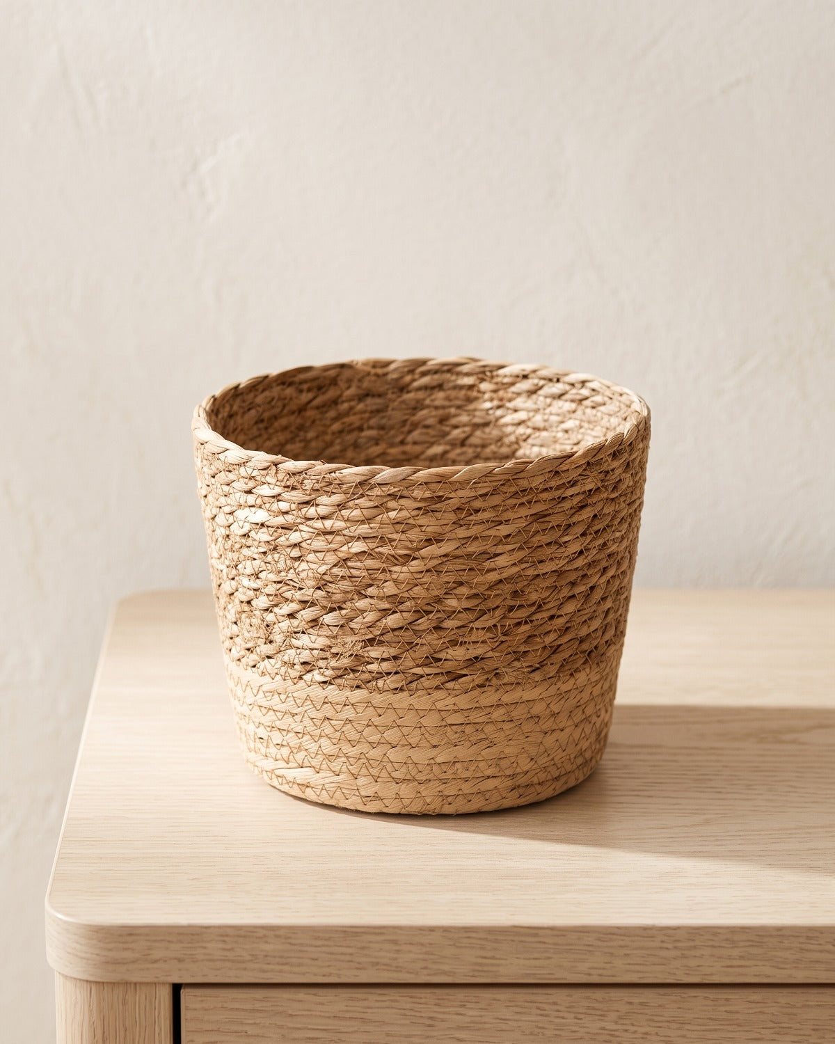 Woven seagrass plant basket, size S, empty on a pale oak table