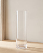 A clear acrylic cylinder vase, empty, on a pale oak table
