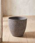 Stone stone effect plant pot standing empty on pale oak floorboards against an off-white plaster wall